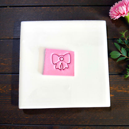 Pink clay slab with bow charm impression on white background