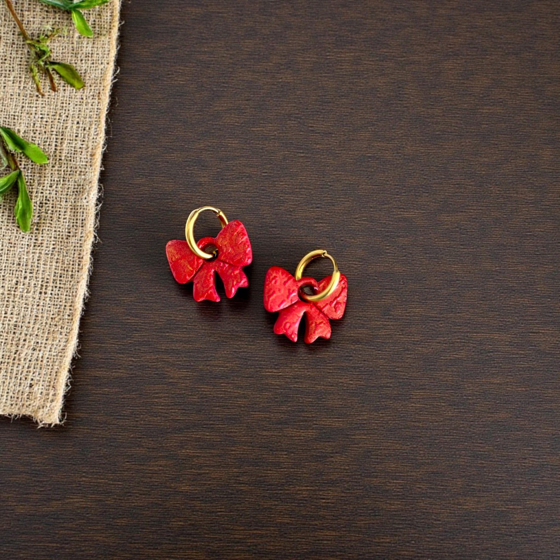 Pair of red bow clay charms on dark wood with burlap