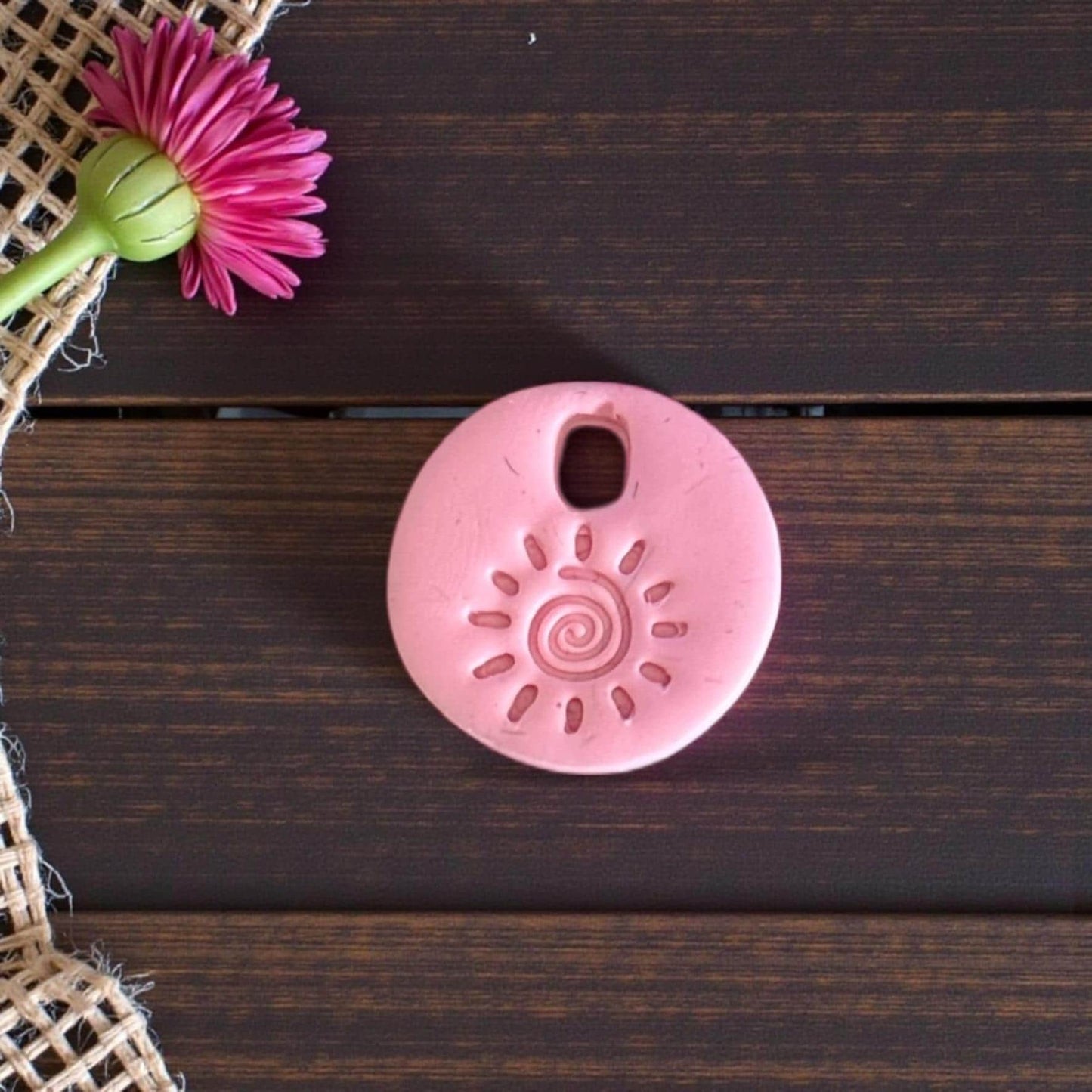 Pink round sun swirl charm on dark wood