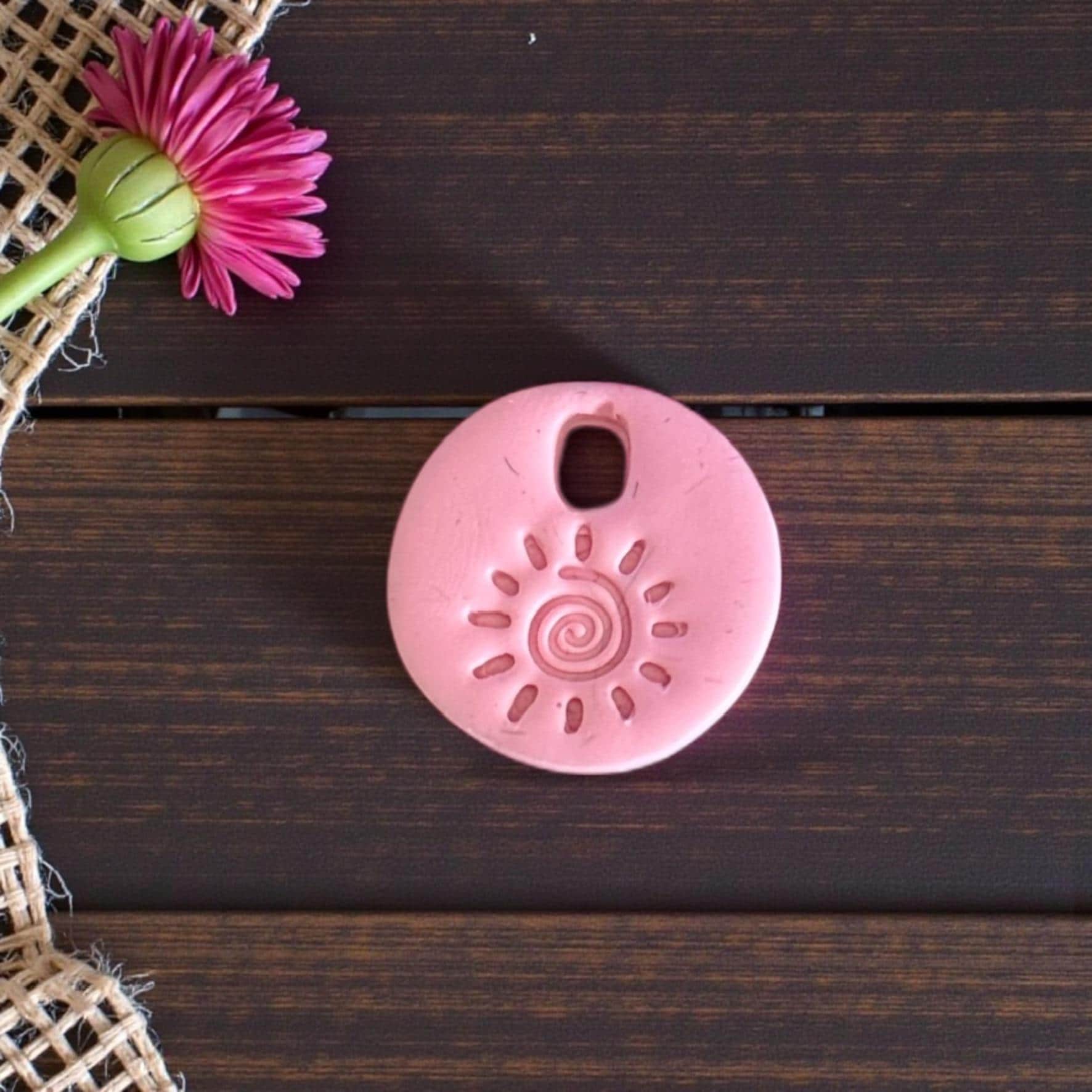 Pink round sun swirl charm on dark wood