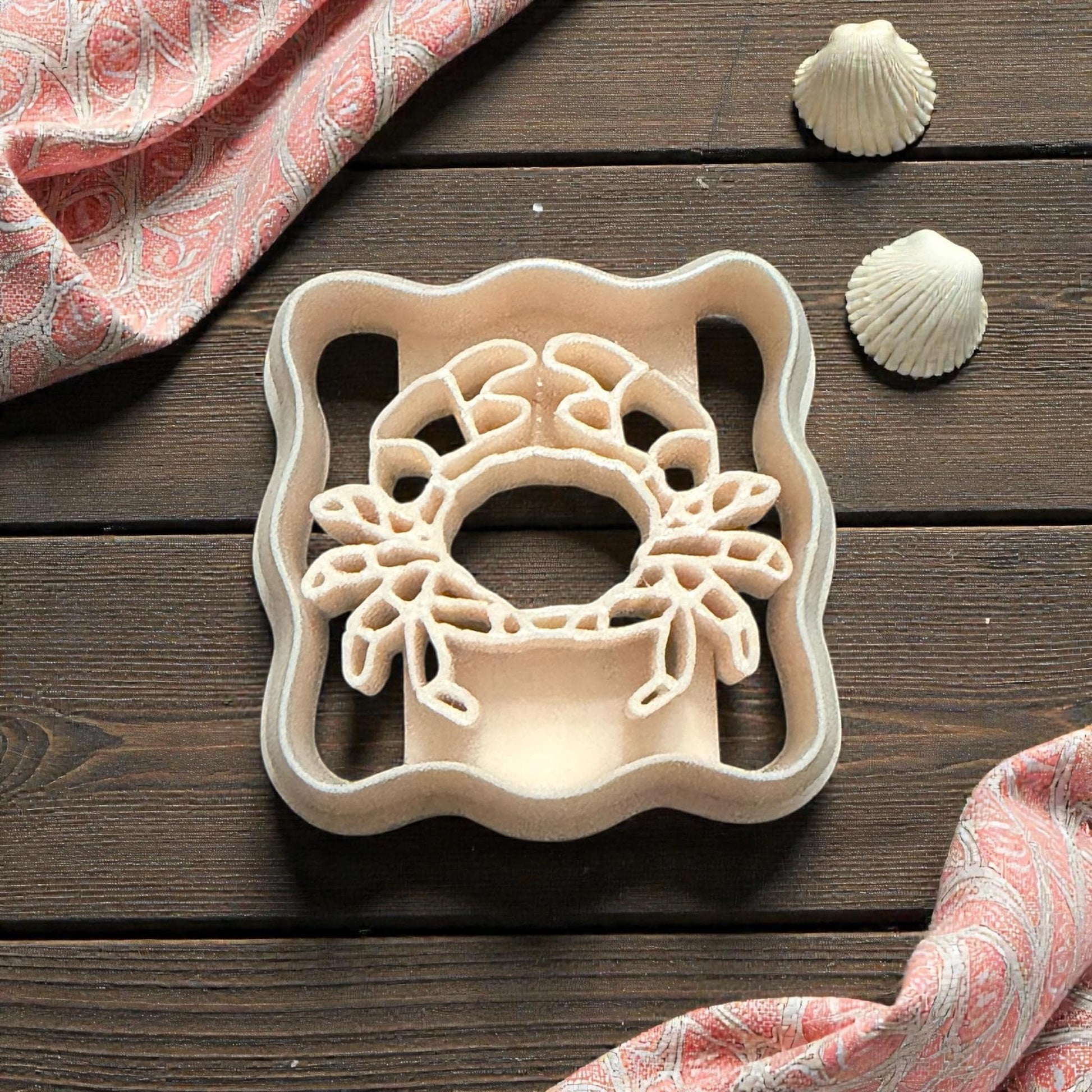 scalloped crab cutter on wooden surface with shells and pink fabric