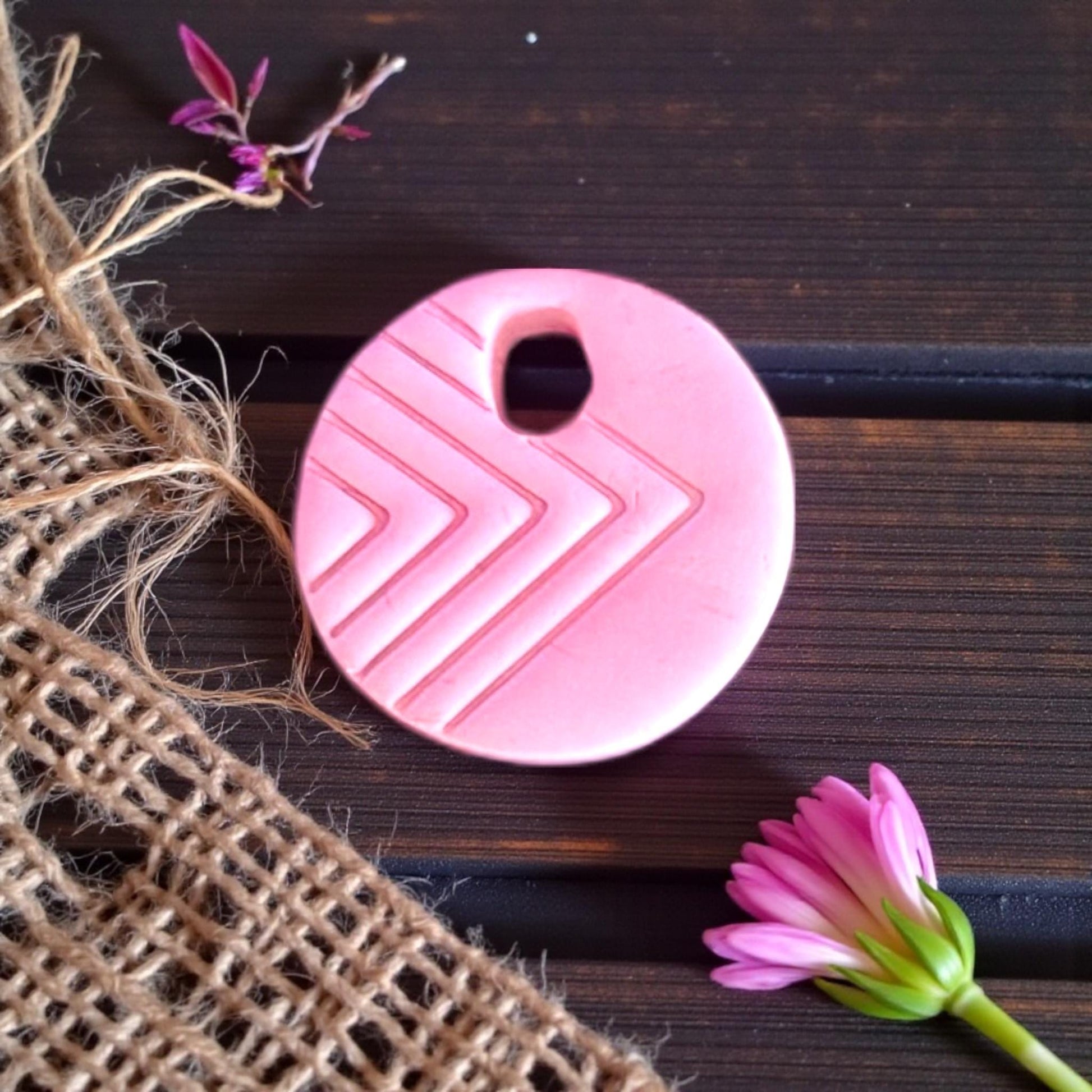 pink round charm with arrow lines resting on burlap
