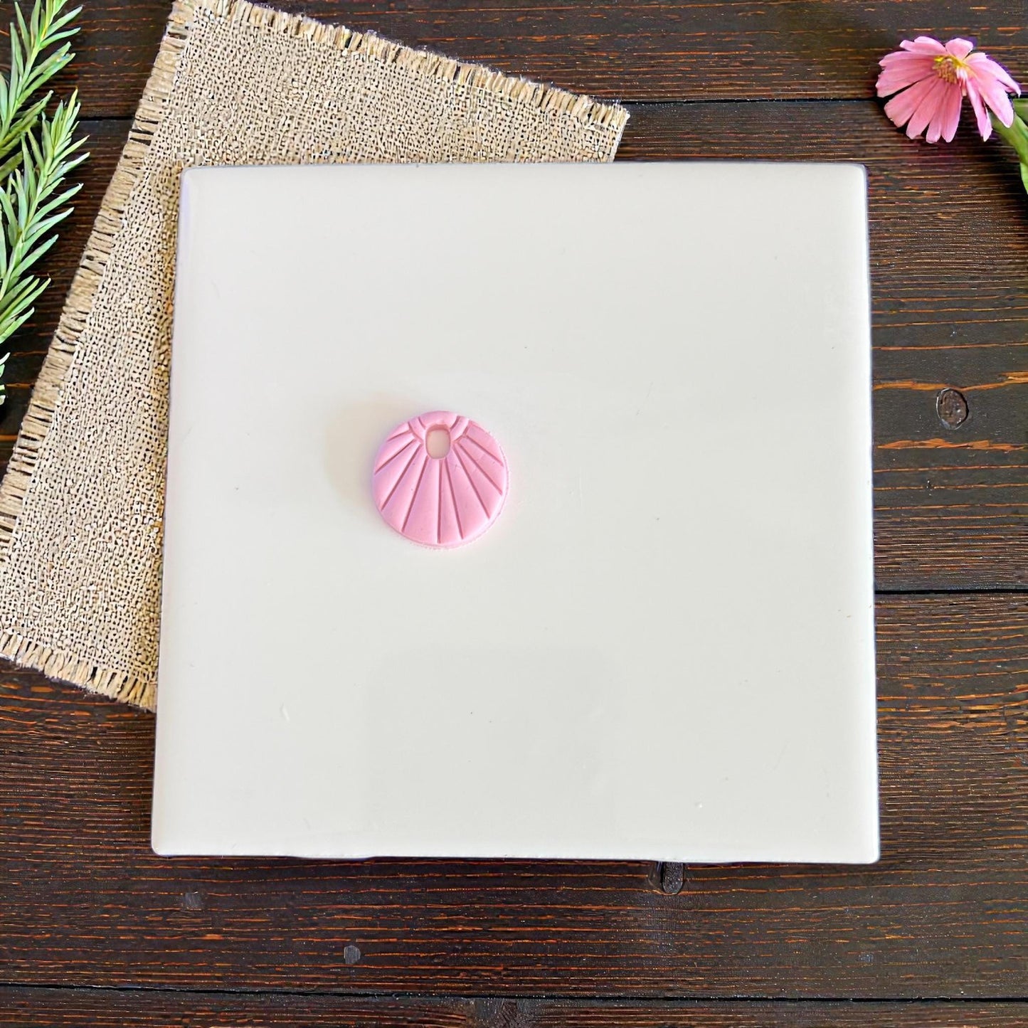 Pink sunburst charm centered on white tile with burlap