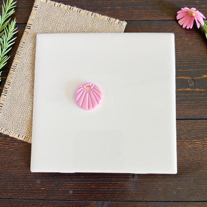 Pink sunburst charm centered on white tile with burlap