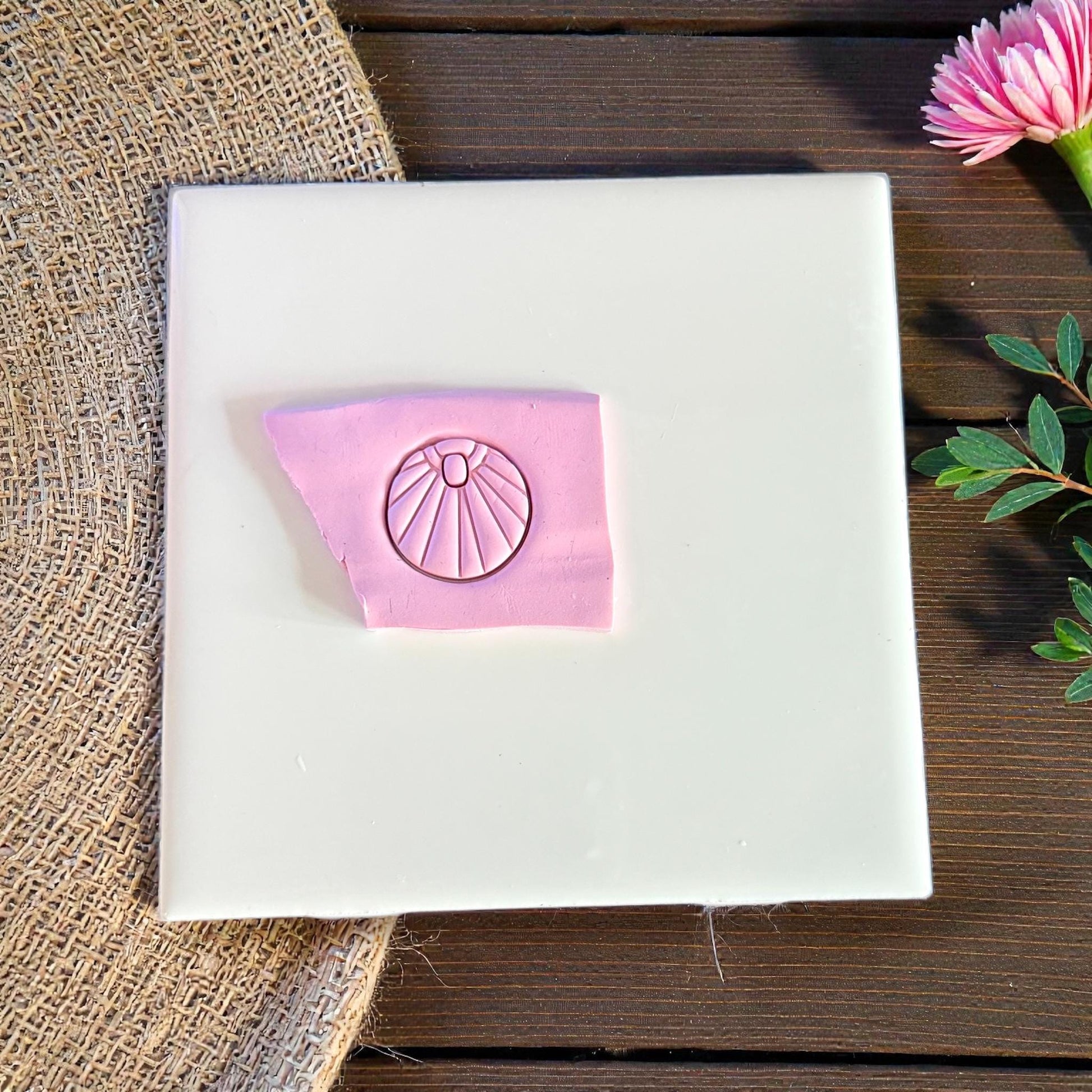 Pink clay impression of sunburst charm on white tile