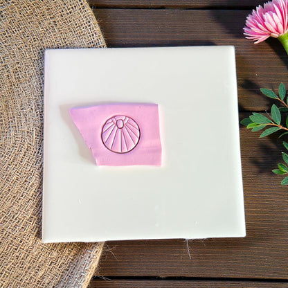 Pink clay impression of sunburst charm on white tile