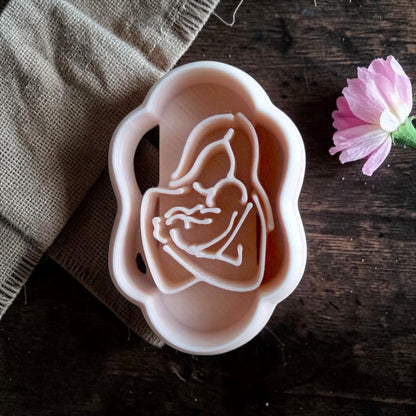 Mother and baby silhouette polymer clay cutter closeup on dark wood with pink flower
