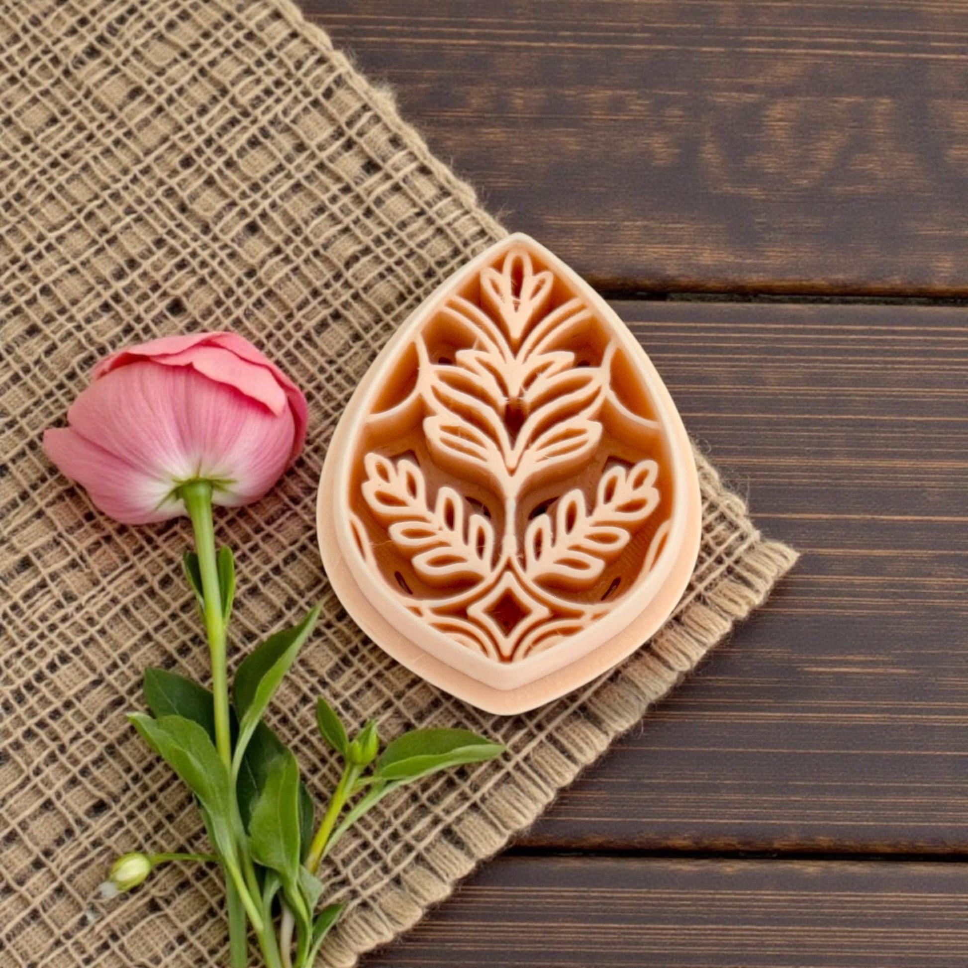 Teardrop botanical polymer clay cutter with floral leaf design on burlap fabric