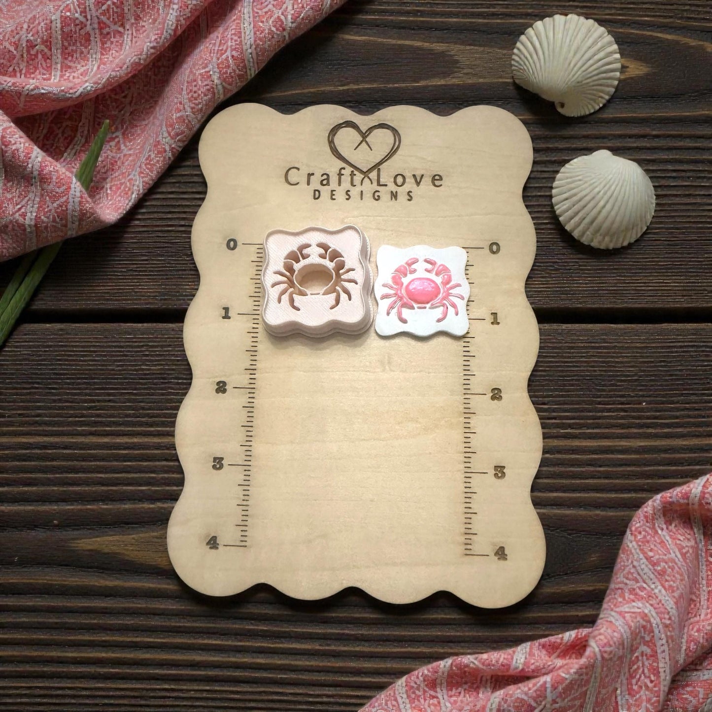 scalloped crab cutter and imprint on wooden size board with shells and pink fabric