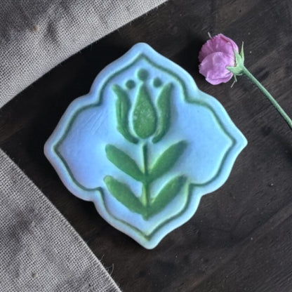Finished blue clay charm with folk tulip design on linen fabric