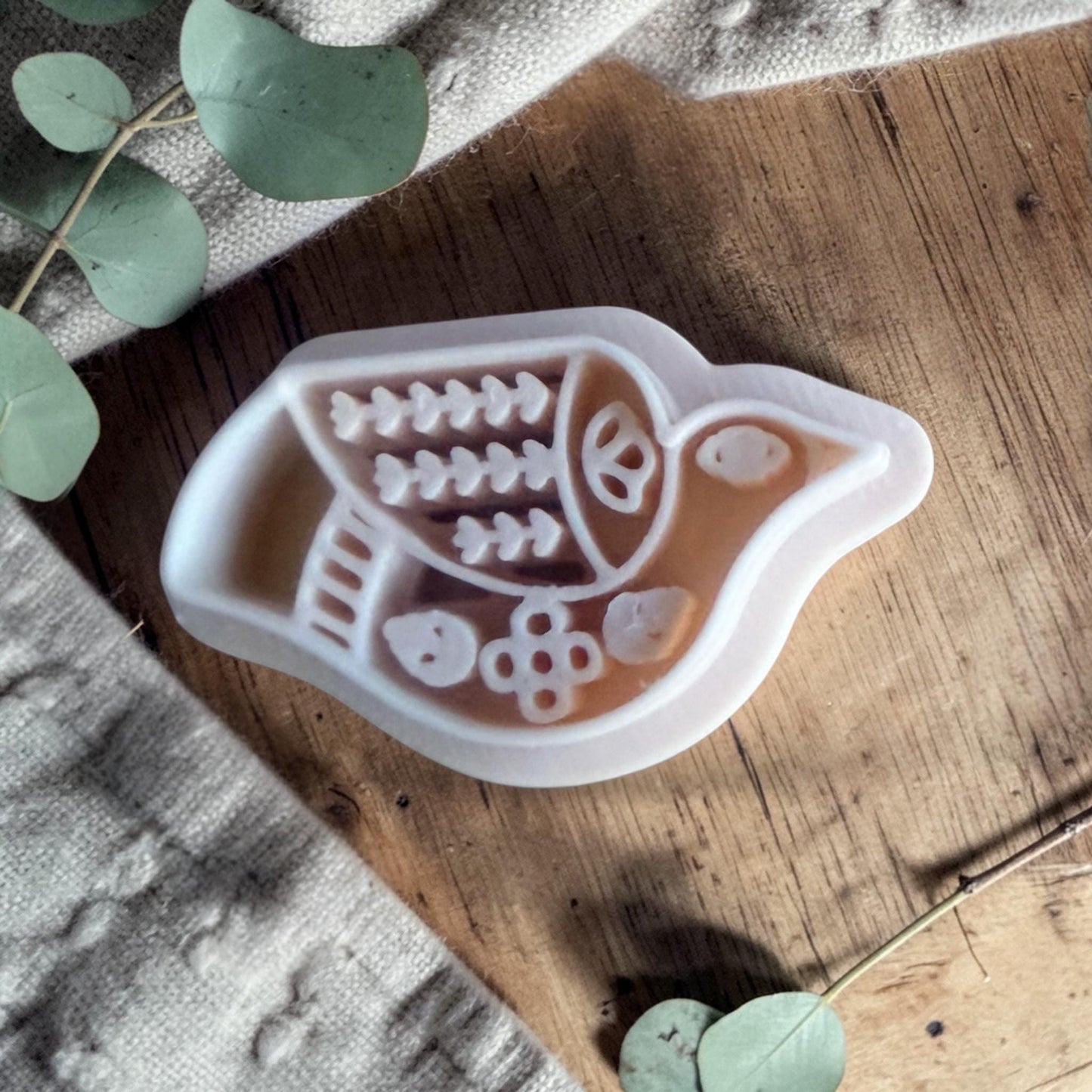 white folk bird polymer clay cutter resting on wood table with eucalyptus leaves