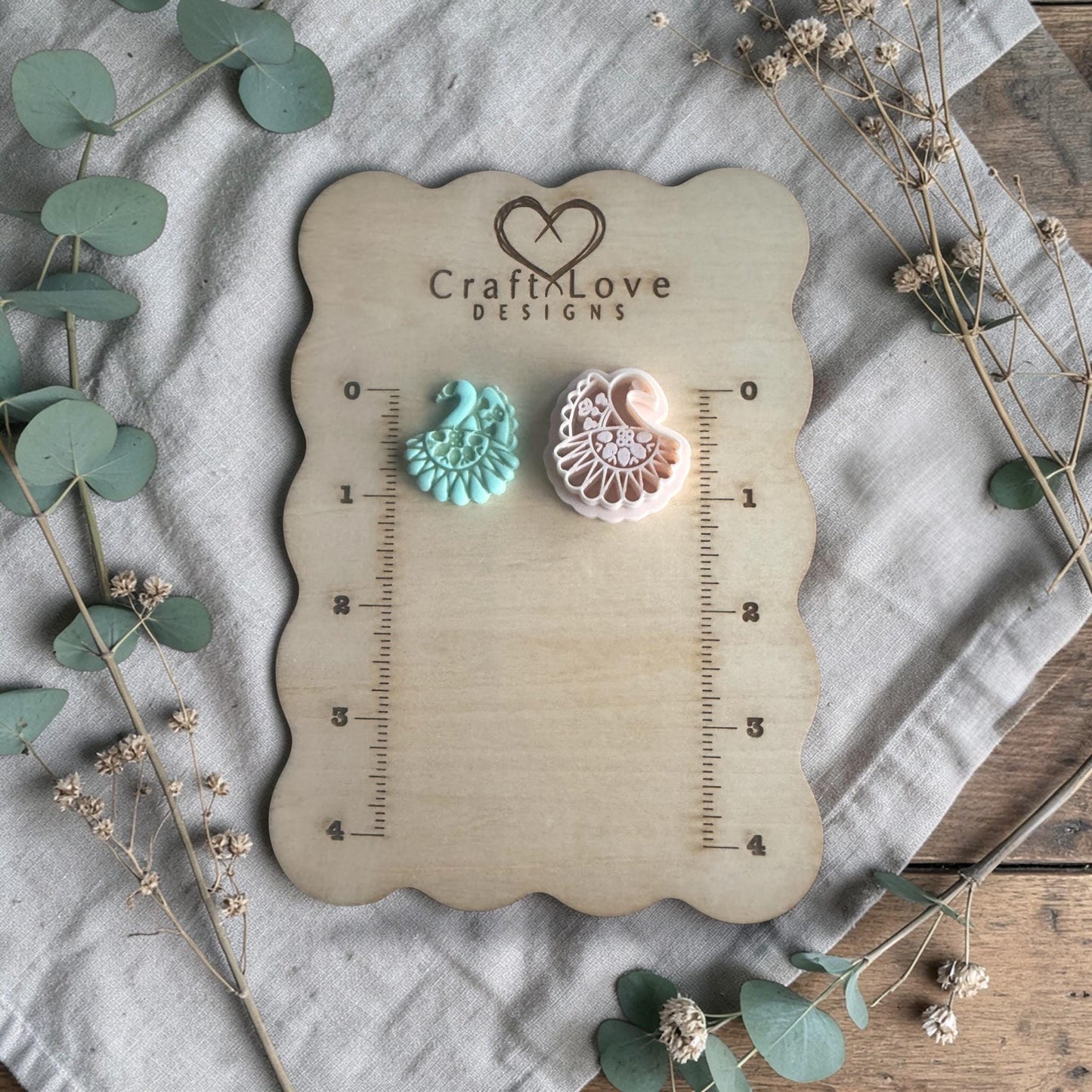 turquoise clay peacock charm and white cutter displayed on Craft Love Designs ruler board