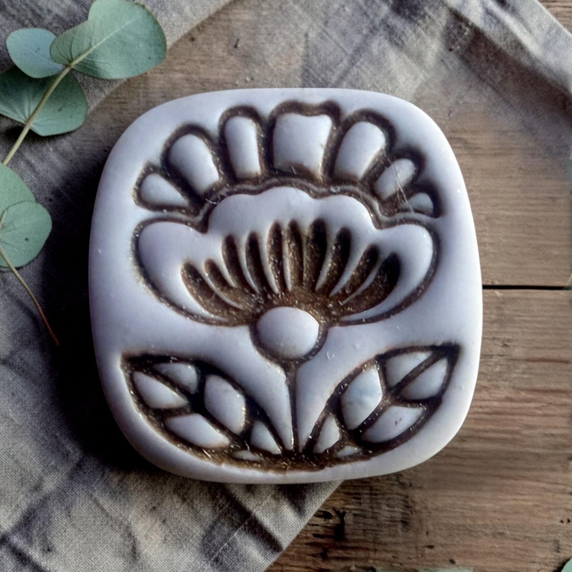 finished clay charm showing embossed folk flower design inside rounded square shape