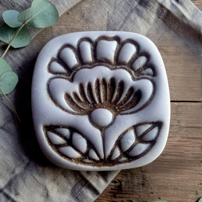 finished clay charm showing embossed folk flower design inside rounded square shape