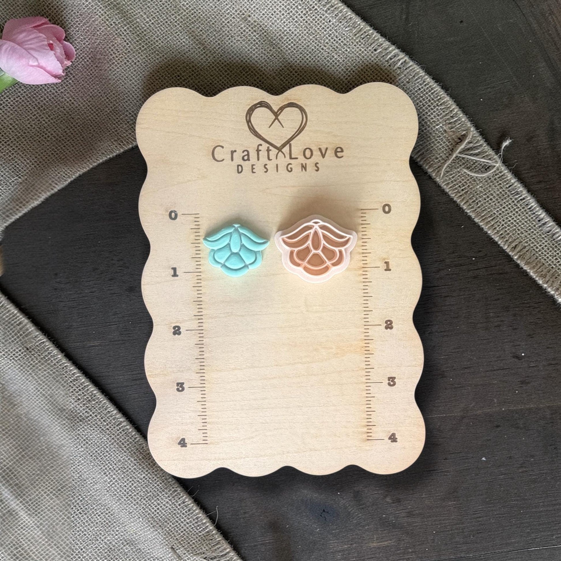 Two small flower shapes side by side on the wooden board, one finished clay piece and one polymer clay cutter showing the design.