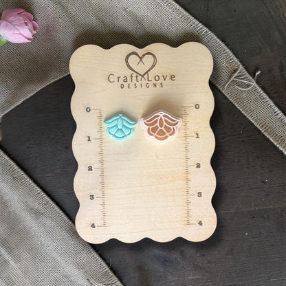 Two small flower shapes side by side on the wooden board, one finished clay piece and one polymer clay cutter showing the design.
