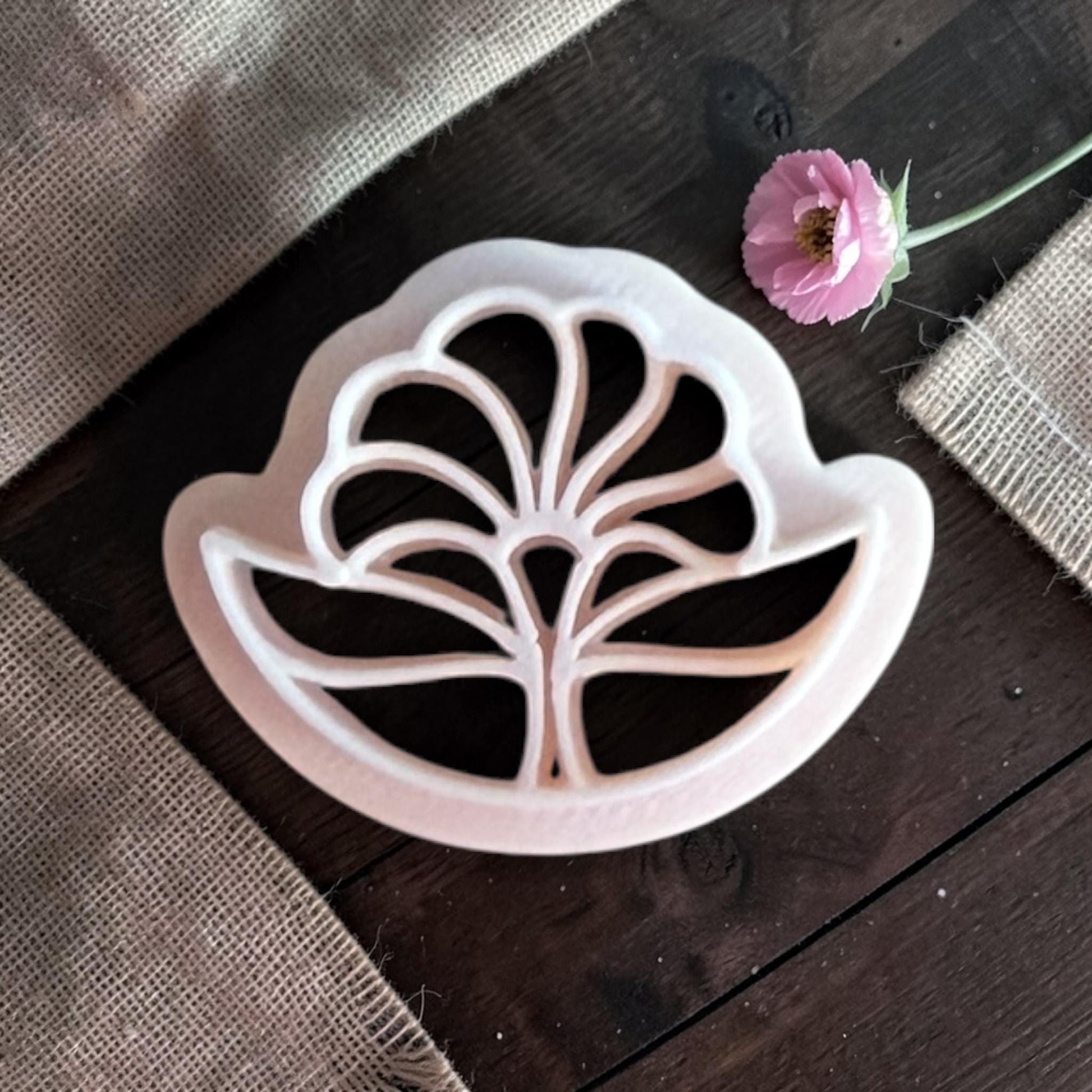 Top-down view of a beige 3D-printed polymer clay cutter in a stylized Art Deco flower shape with sharp, symmetrical petals.