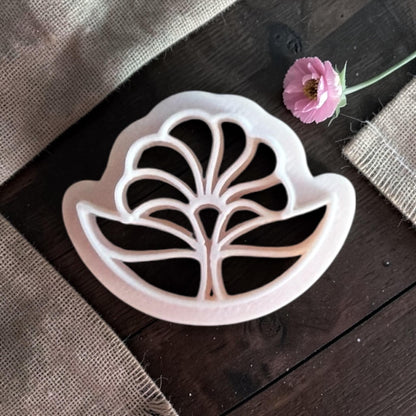 Top-down view of a beige 3D-printed polymer clay cutter in a stylized Art Deco flower shape with sharp, symmetrical petals.