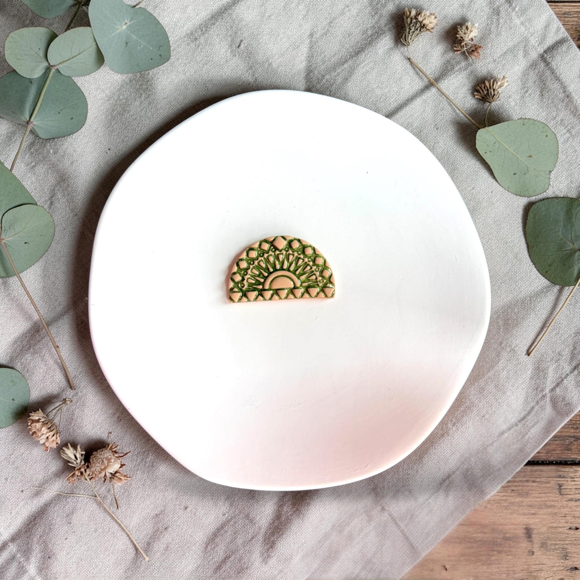 Finished clay arch piece in green showing detailed geometric fan and sunburst texture on a white plate.