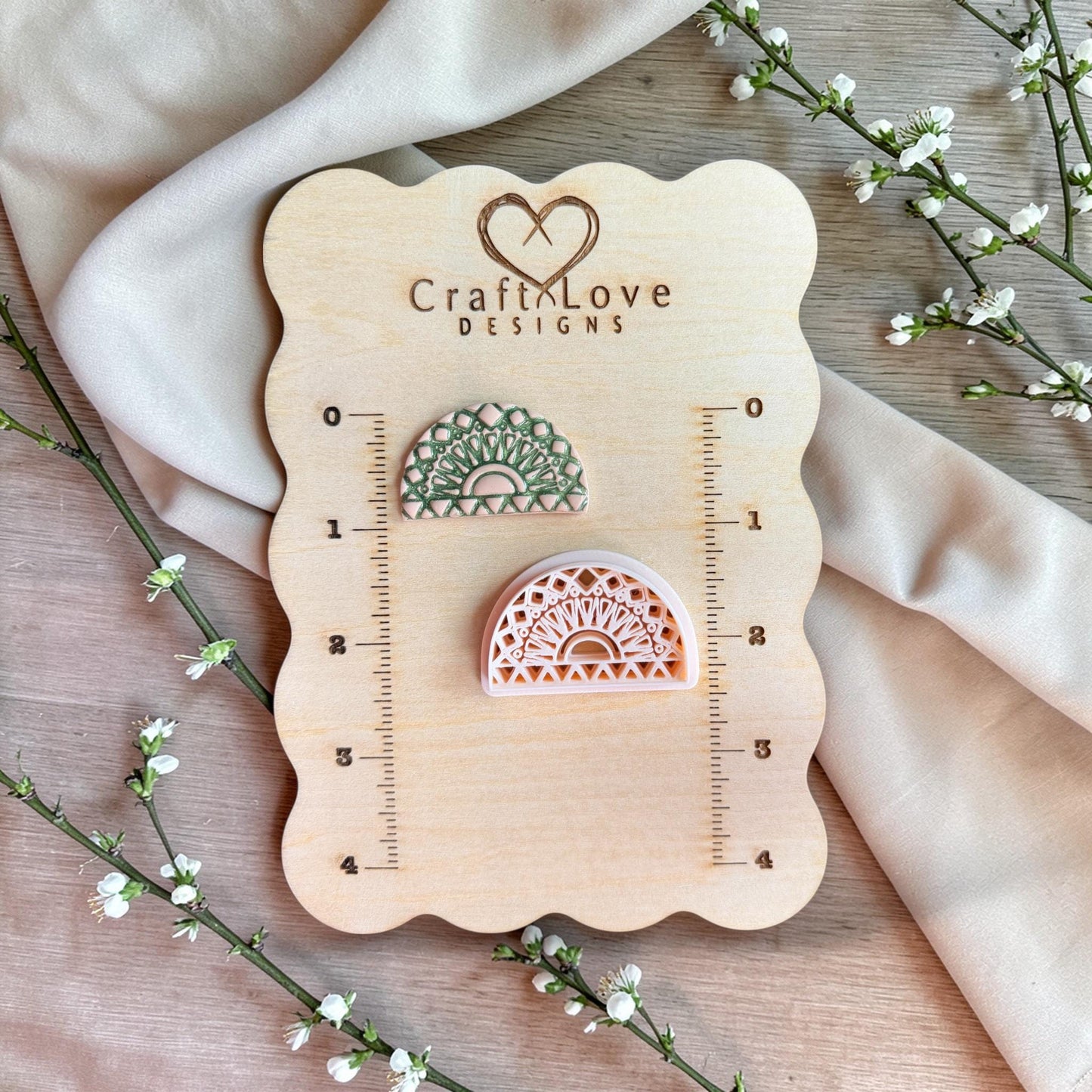 Polymer clay cutter and finished clay piece displayed on a wooden measuring board with ruler markings and floral accents.