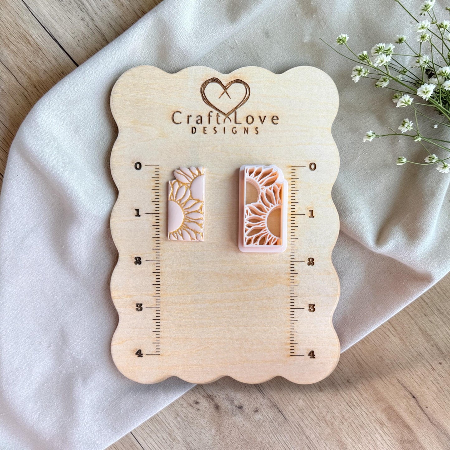 Two rectangular pieces on a wooden measuring board, one sunflower polymer clay cutter and one finished clay piece with gold detailing.