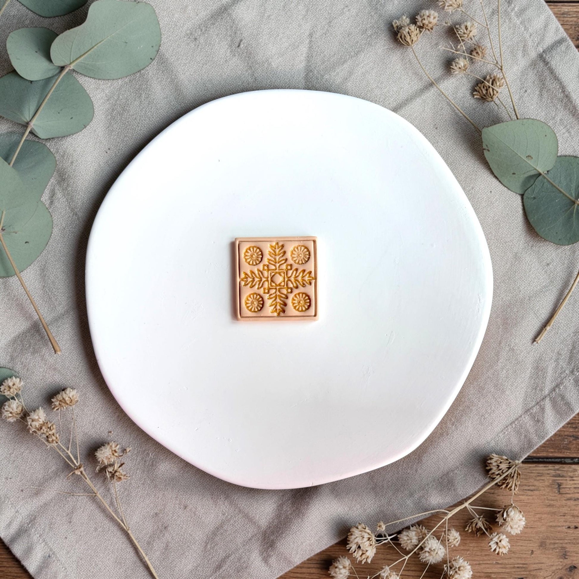 Finished clay piece with gold-highlighted Nordic floral tile design centered on a white plate.