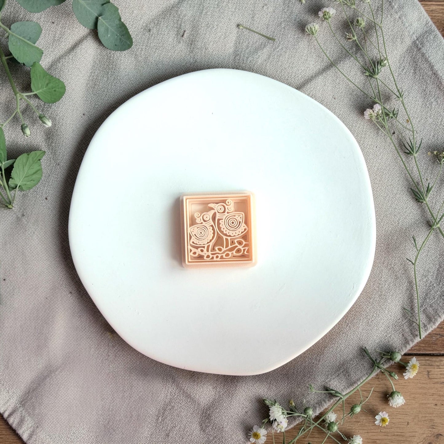 Square polymer clay cutter with two Scandinavian-style birds displayed on a white plate with soft greenery.