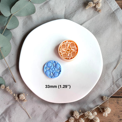 Polymer clay cutter and finished clay pieces side by side with size text 33mm on a white plate with dried florals.