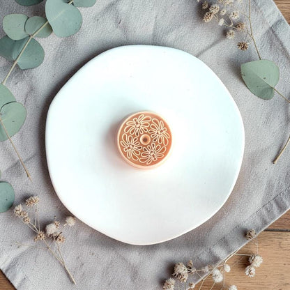 Round polymer clay cutter with abstract boho flower pattern placed on a white plate with neutral fabric and dried florals.