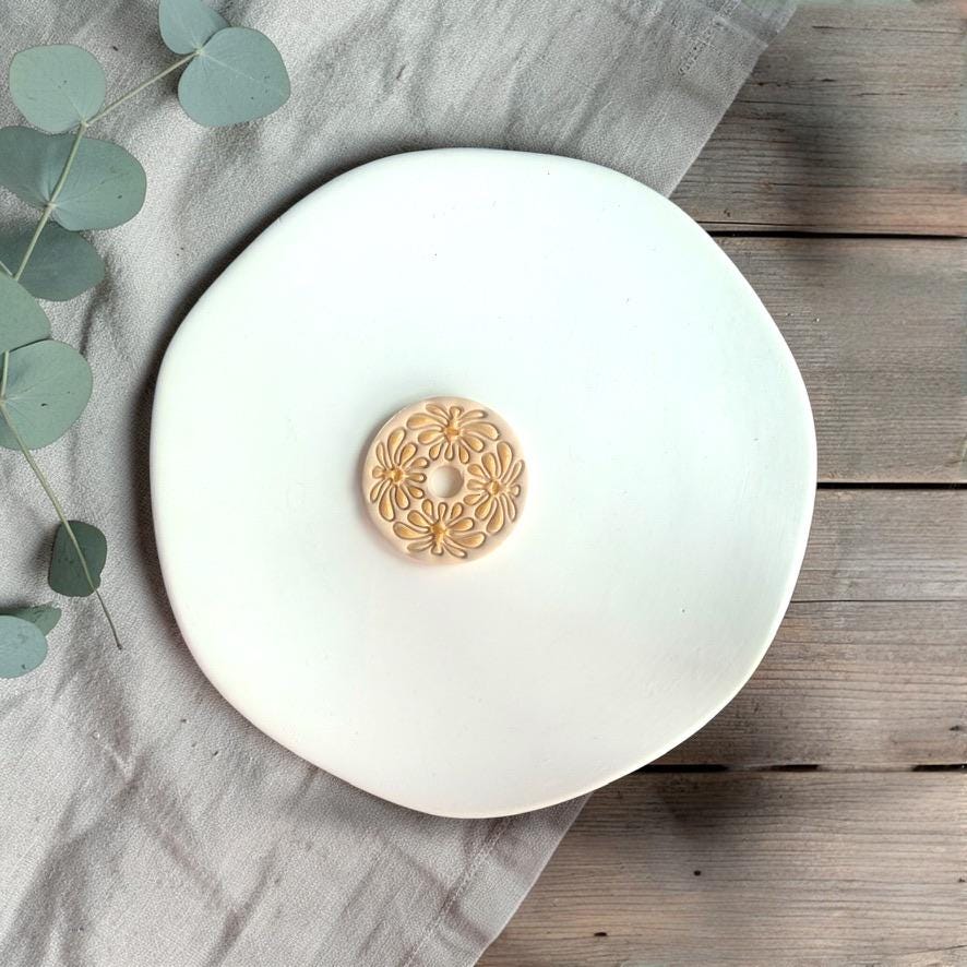 Single finished clay piece with abstract flower pattern centered on a white plate with soft neutral styling.