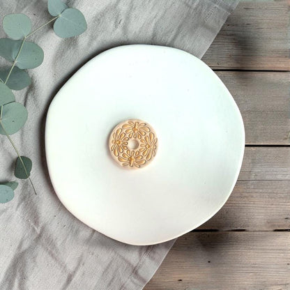 Single finished clay piece with abstract flower pattern centered on a white plate with soft neutral styling.