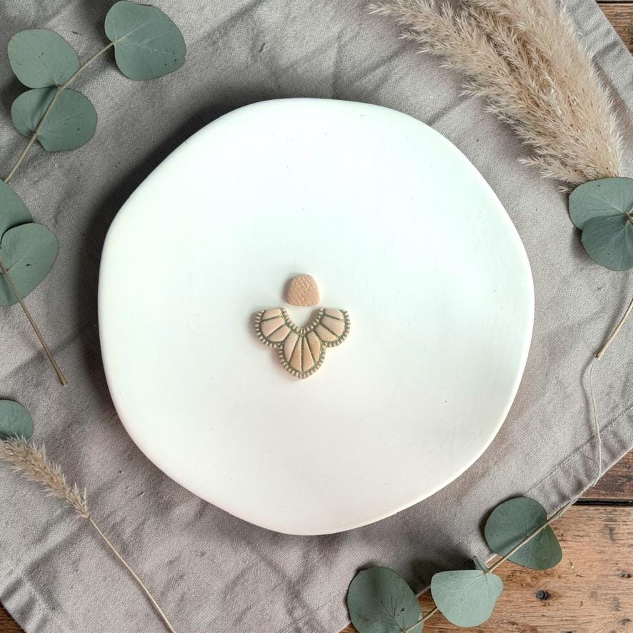 Finished clay earring with textured top stud and boho fan wing drop displayed on a white plate with neutral styling.