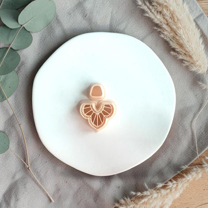 Clay cutter with scalloped fan wing design and small top piece placed on a white plate with neutral fabric and dried grass.
