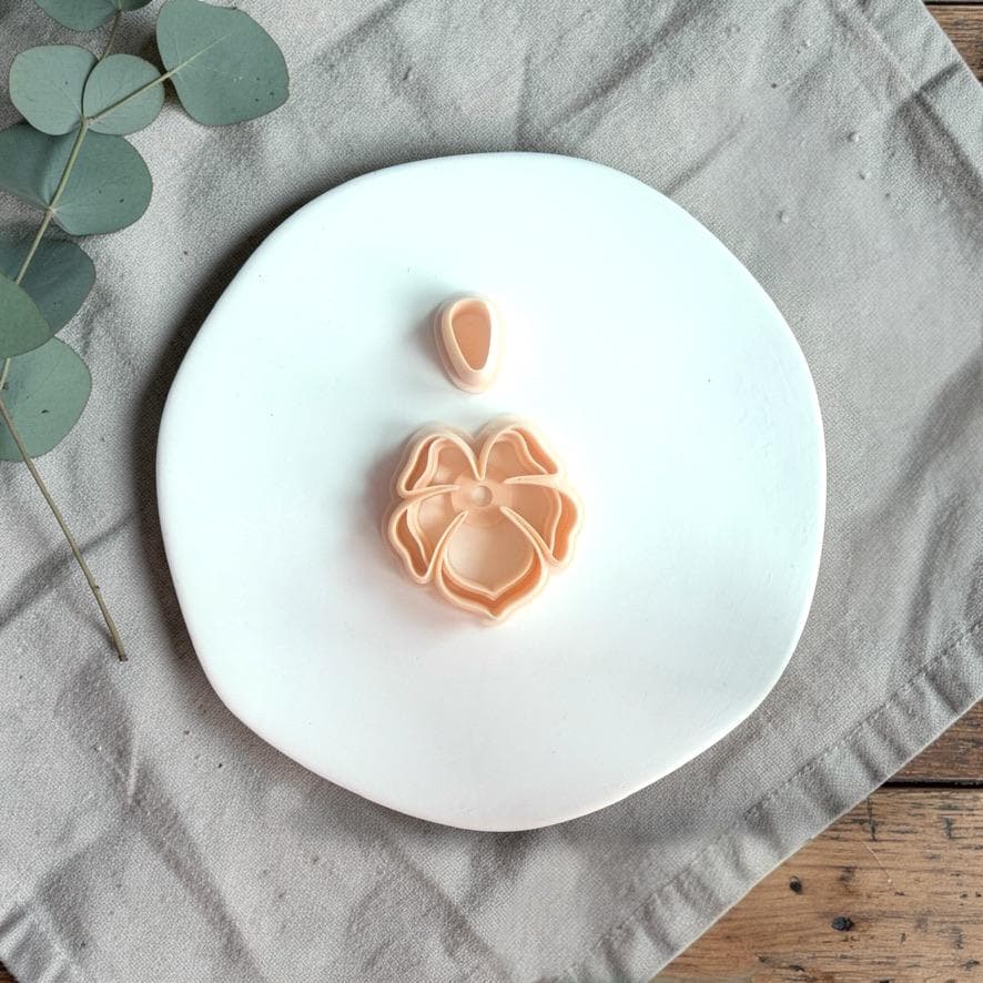 Tropical flower clay cutter with layered petal design and separate top piece placed on a white plate with neutral fabric.
