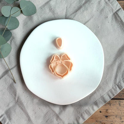 Tropical flower clay cutter with layered petal design and separate top piece placed on a white plate with neutral fabric.