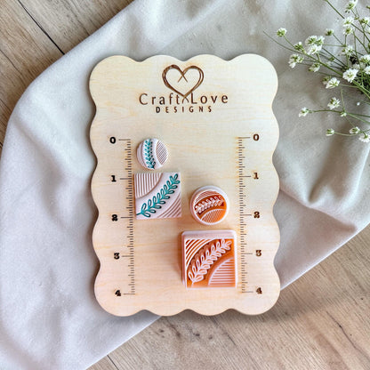 Square and circle polymer clay cutters with botanical leaf pattern displayed on a wooden measuring board with ruler markings.
