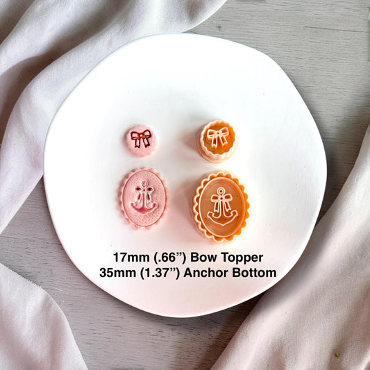 Finished polymer clay pieces with anchor and bow design in pastel pink and orange tones on white plate.