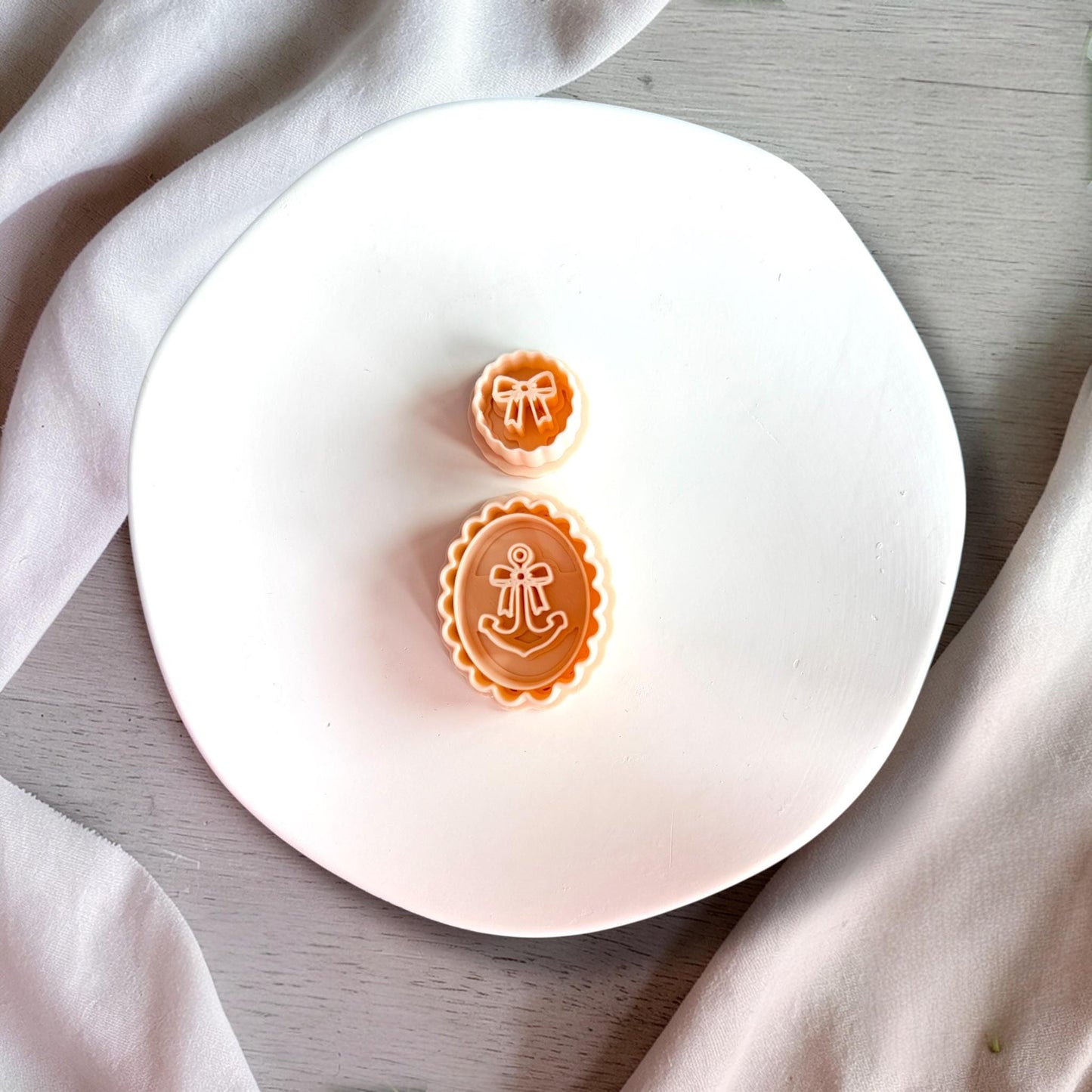 Nautical anchor and bow clay cutters placed on white plate with neutral fabric background showing clean detailed design.