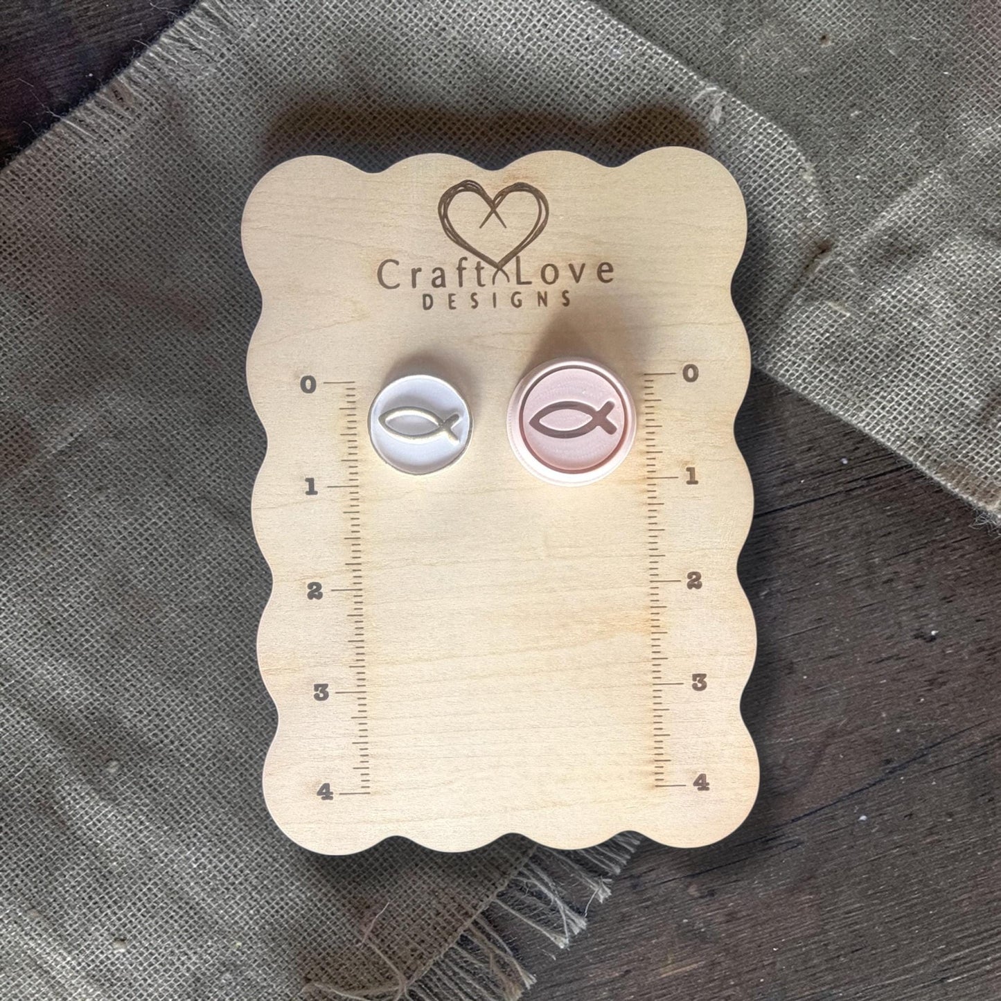 Two Christian fish polymer clay cutters in different sizes on linen fabric