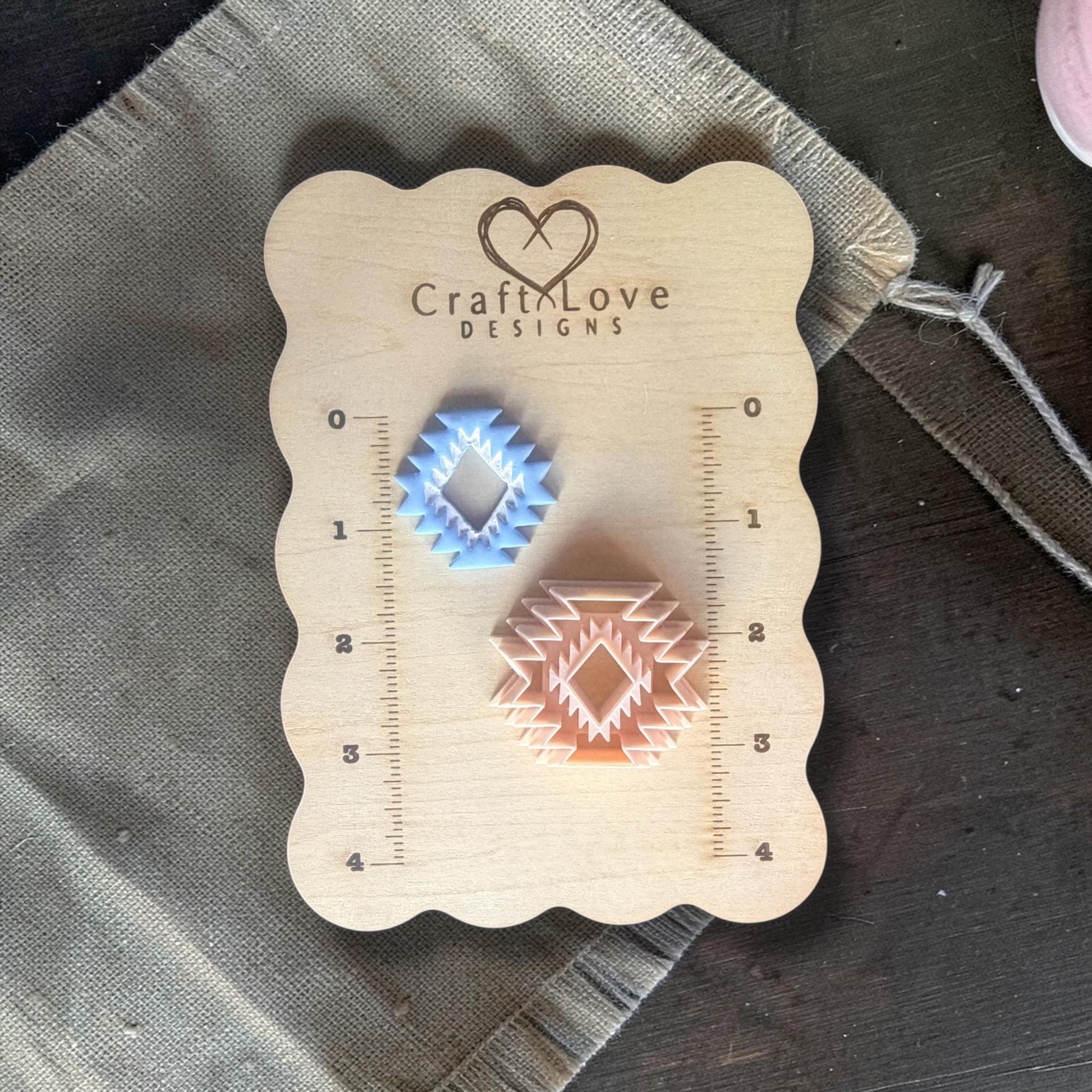 Two finished aztec clay charms in blue and peach on ruler board