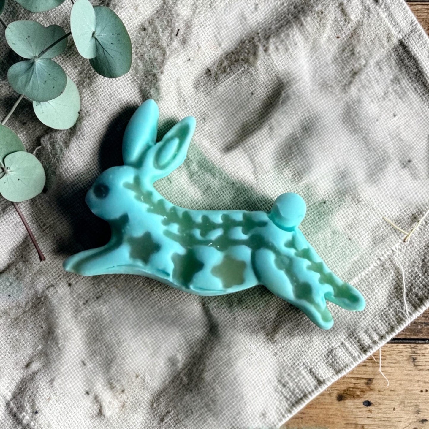 turquoise clay folk rabbit charm with embossed decorative pattern on linen fabric