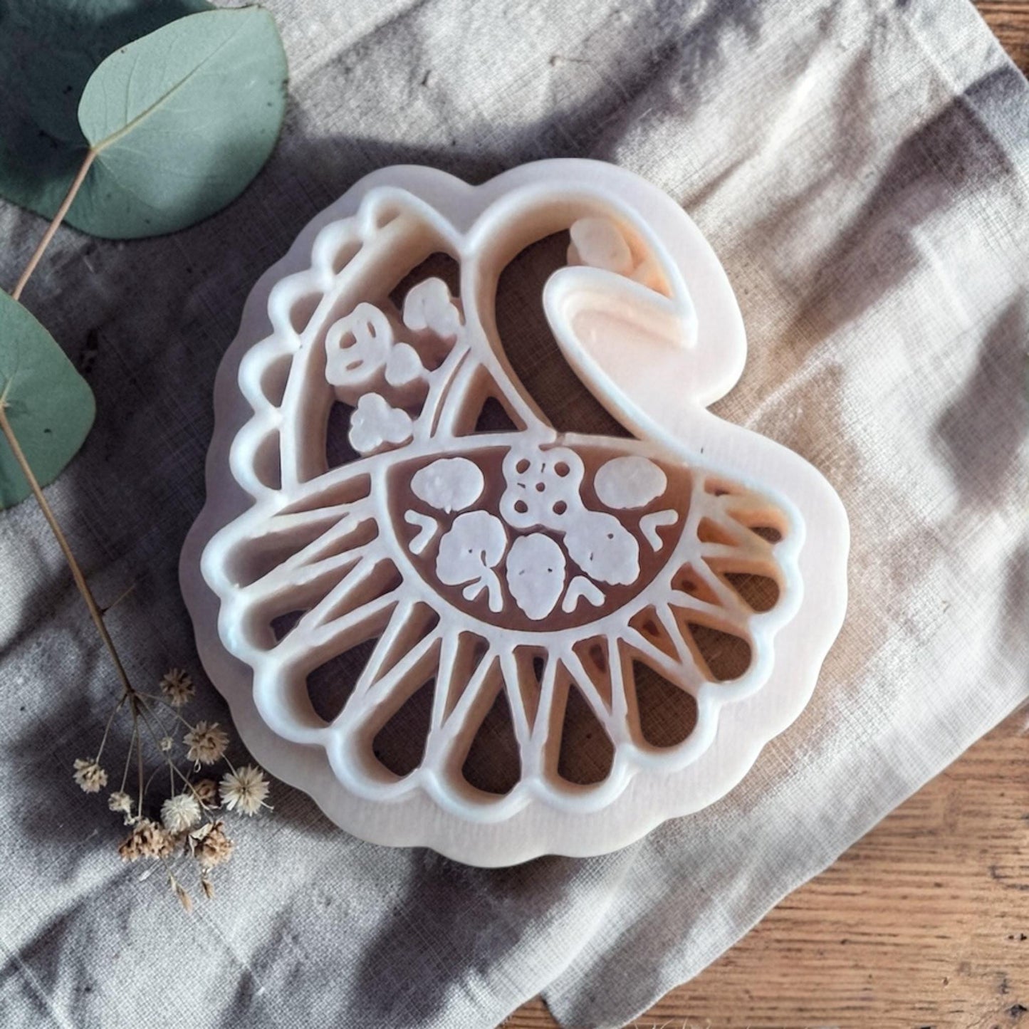 white peacock clay cutter with floral and feather pattern on linen background