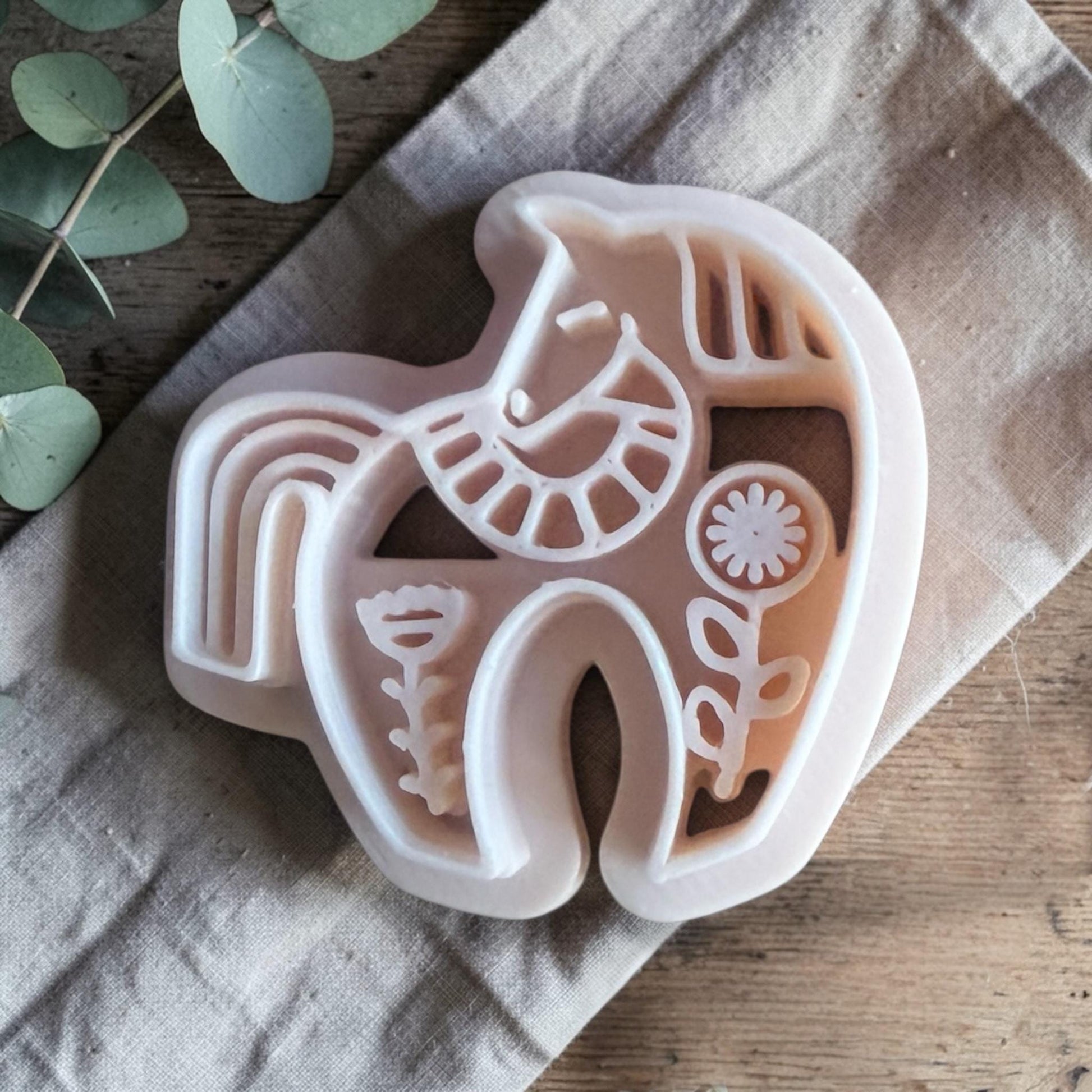 white polymer clay horse cutter with folk art details on neutral fabric background
