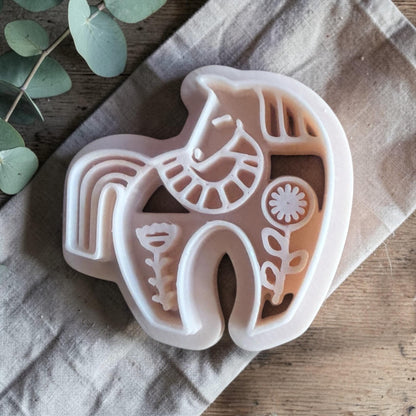 white polymer clay horse cutter with folk art details on neutral fabric background