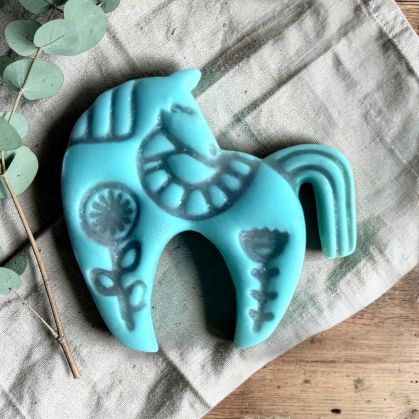 turquoise clay folk horse charm with embossed Scandinavian floral pattern on linen