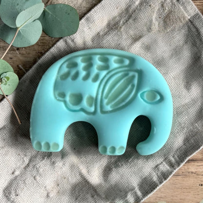 turquoise clay elephant charm with embossed folk art details on linen fabric