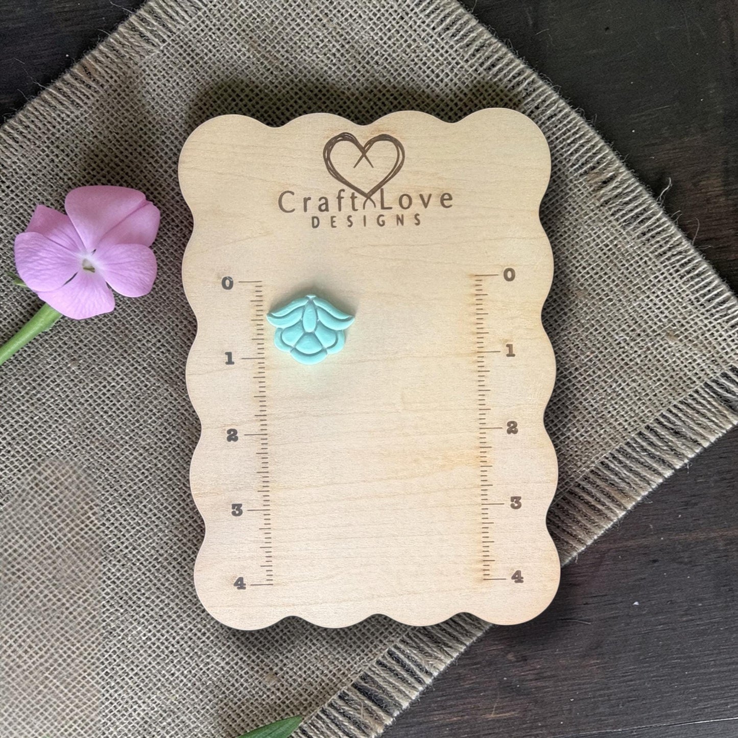 Turquoise clay piece pressed from the floral cutter displayed on a wooden measuring board showing the finished flower design.