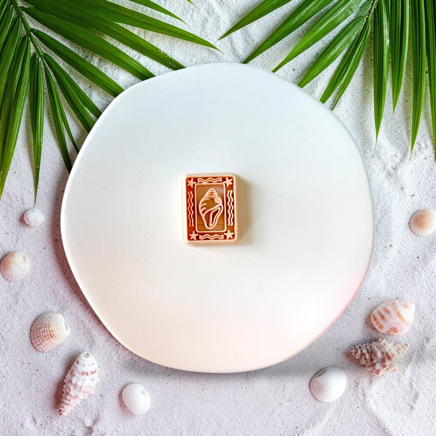 Seashell frame polymer clay cutter on sandy beach background with palm leaves and seashell props
