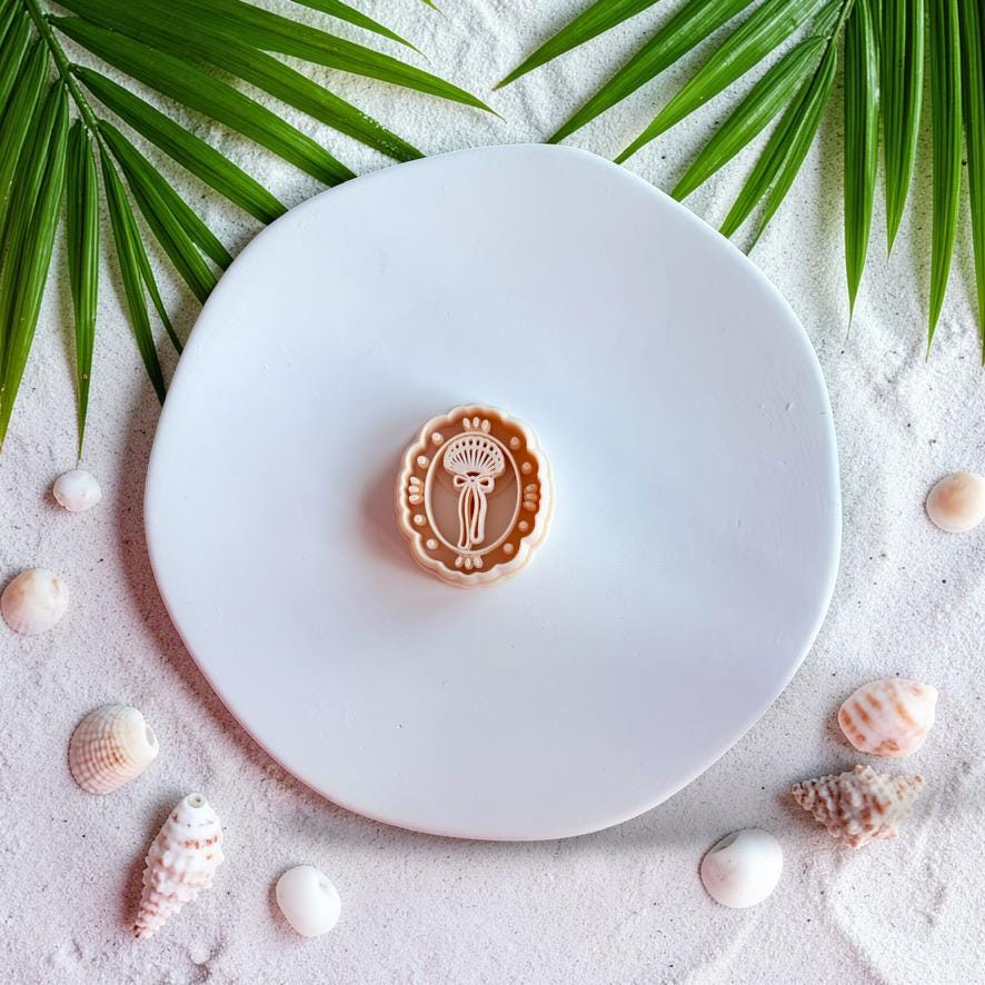Seashell bow polymer clay cutter on sandy beach background with palm leaves and shells