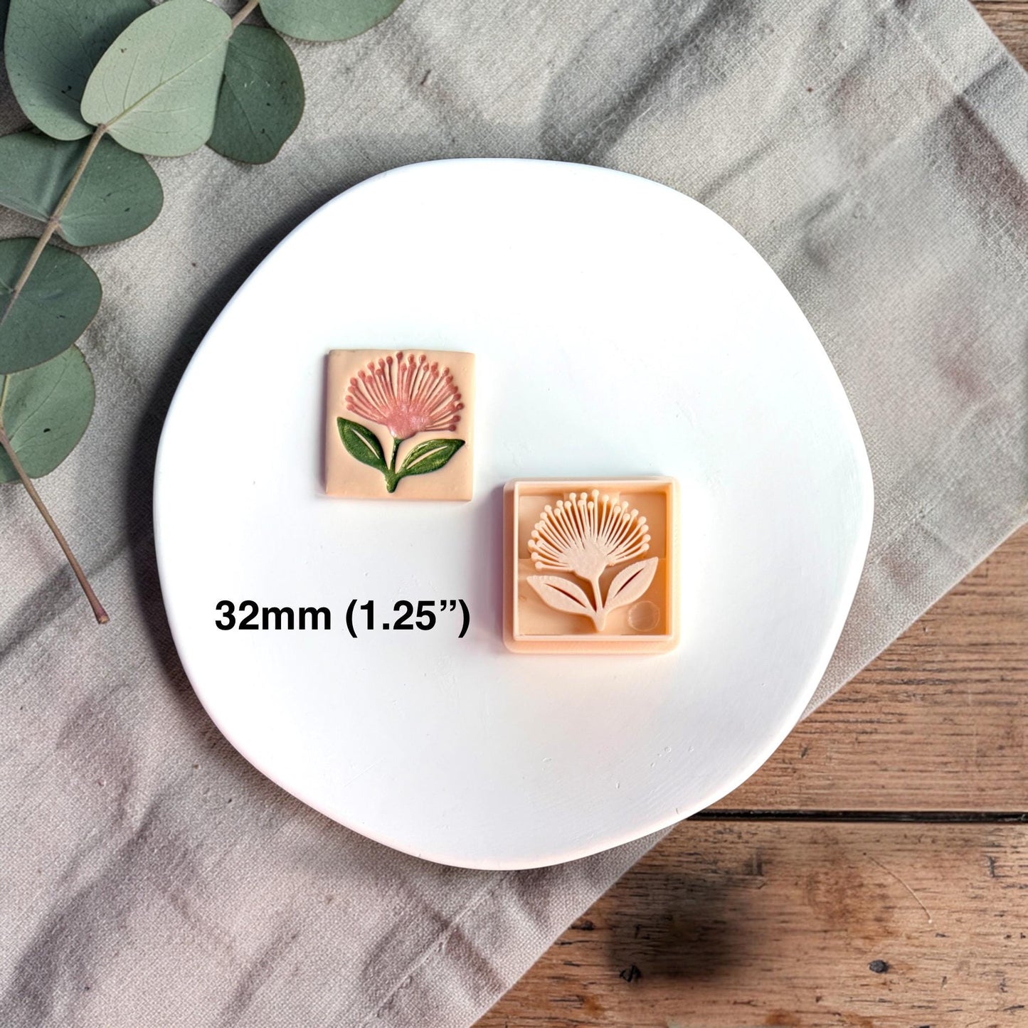 Square polymer clay cutter with pohutukawa flower design displayed on a white round plate with neutral fabric and greenery.